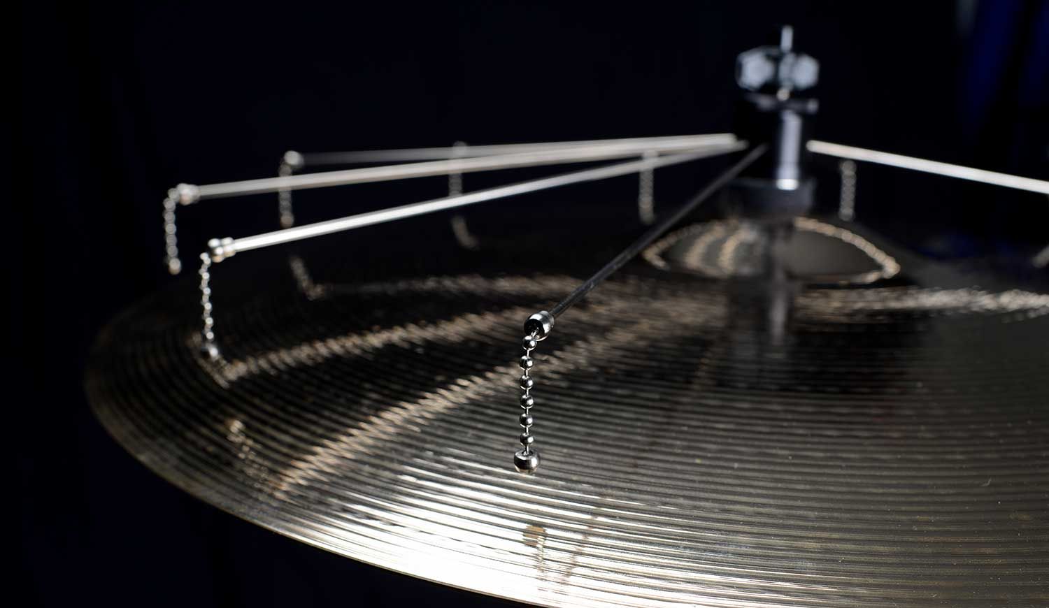 Close-up of a ride cymbal with the Jaspercussion Cymb Size sizzler attachment suspended over it against a dark background. 